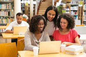 smiling students working with laptop at library